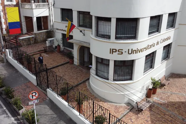 Fachada de la IPS Universitaria de Colombia vista desde un dron: edificio blanco de esquina curva con el nombre de la IPS